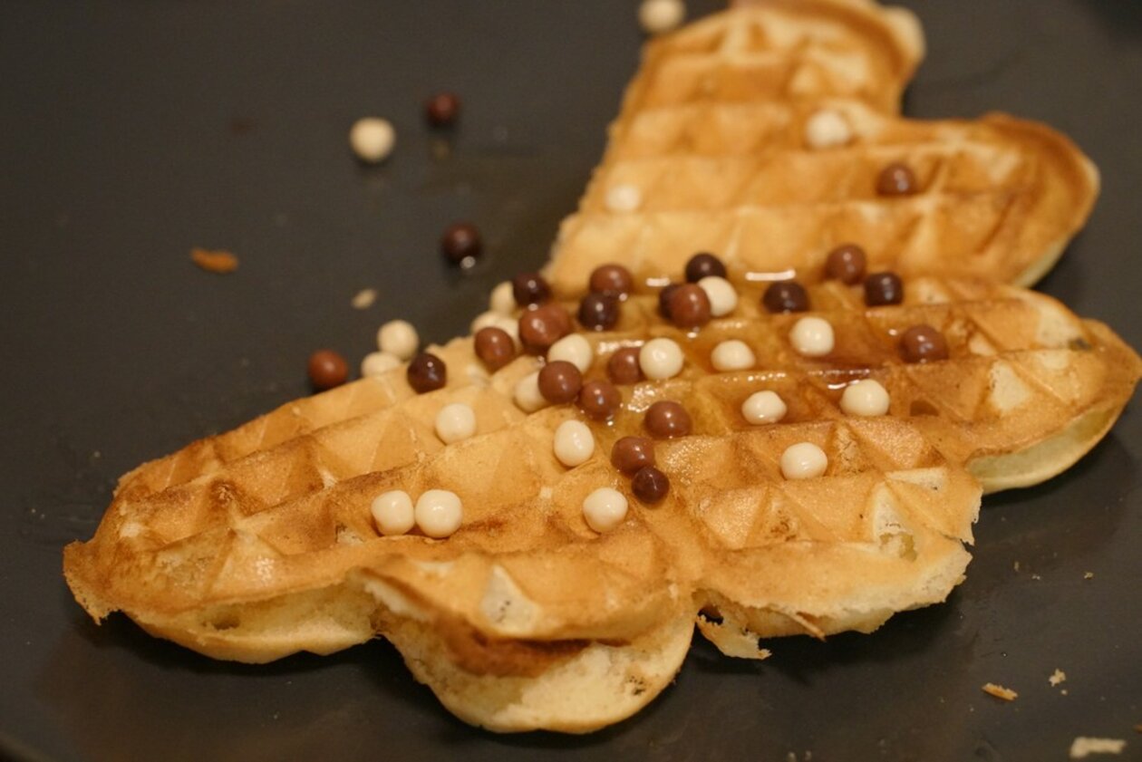 About half a
crispy golden waffle with small chocolate balls on it on a black
plate.